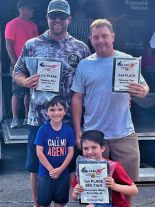 Brad Lail (left) and Daniel Champion are shown with plaques for second place overall and Big Kat of the tournament. In front are Lail’s sons Maximus (left) and Deacon. 