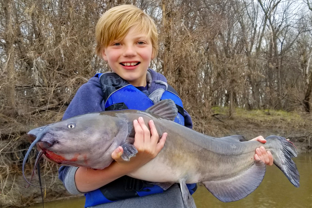 The author’s son Braden holding a very early spring channel catfish. If you notice behind him, the river is full to the top of the cut bank, and plant life is just starting to sprout. This is a time to get out of the current on the OFF current seam to find sluggish catfish.